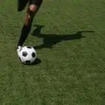 Pernas de uma mulher chutando uma bola em um campo de futebol.